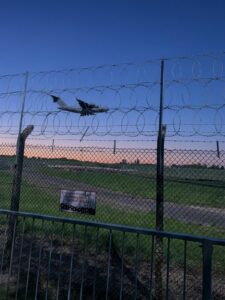 Military transport aircraft descending beyond the Birmingham Airport perimeter in the half-light